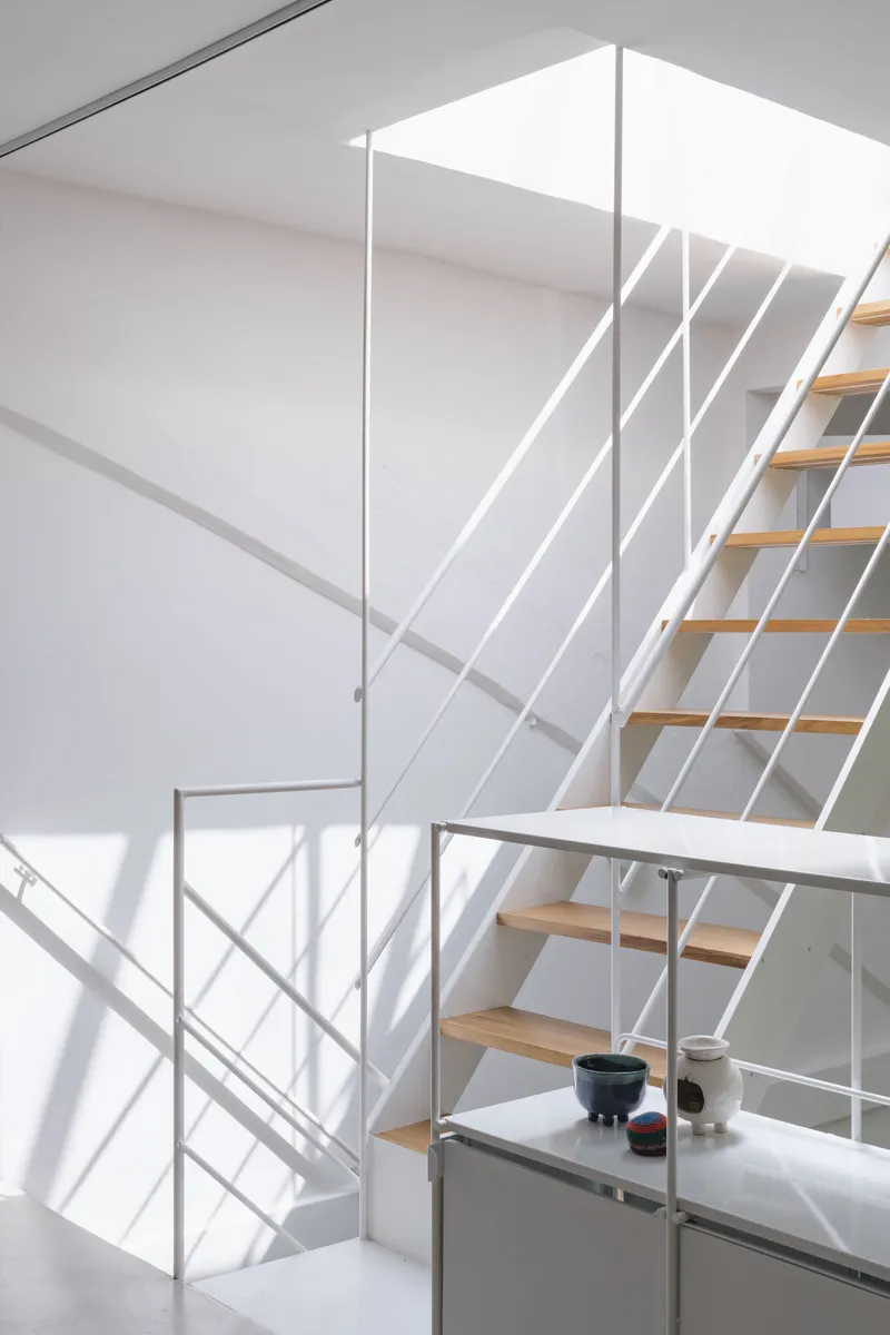 Open timber staircase with white steel railings climbing through a double-height volume in bright daylight