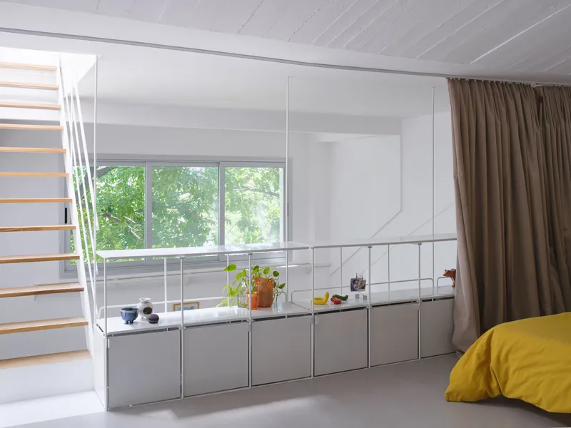 Modular storage system with grey cabinetry below a horizontal window framed by taupe curtains and exposed ceiling joists