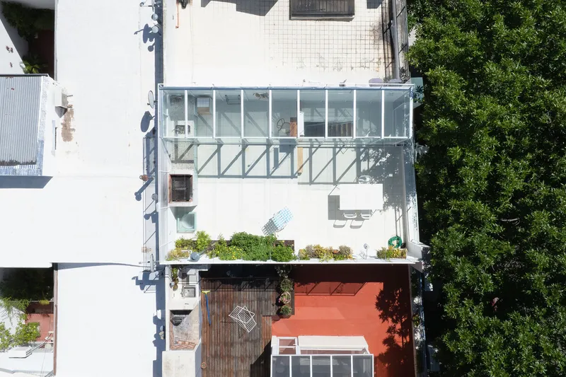 Aerial view of stacked glass volumes on a white facade with planted terrace and adjacent trees