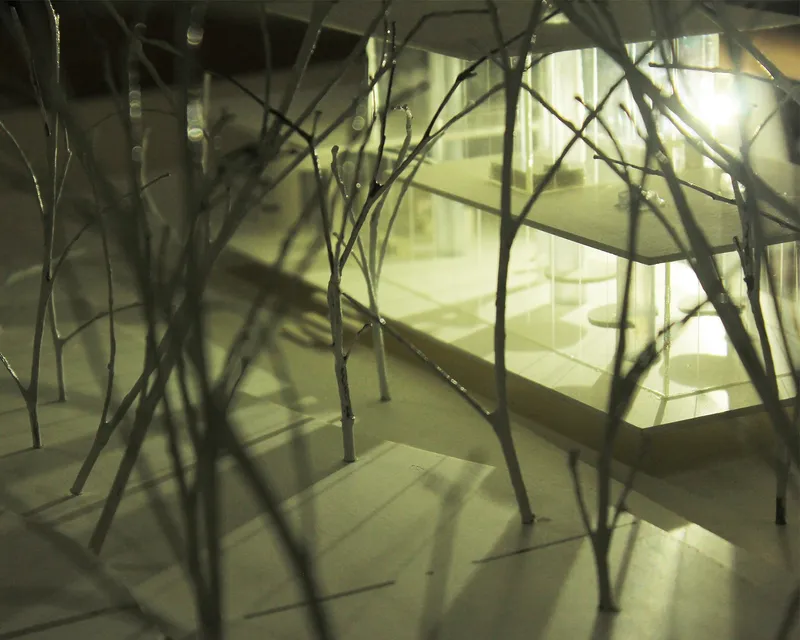 The transparent atelier appears through dense branches, reinforcing its immersive relationship with nature.