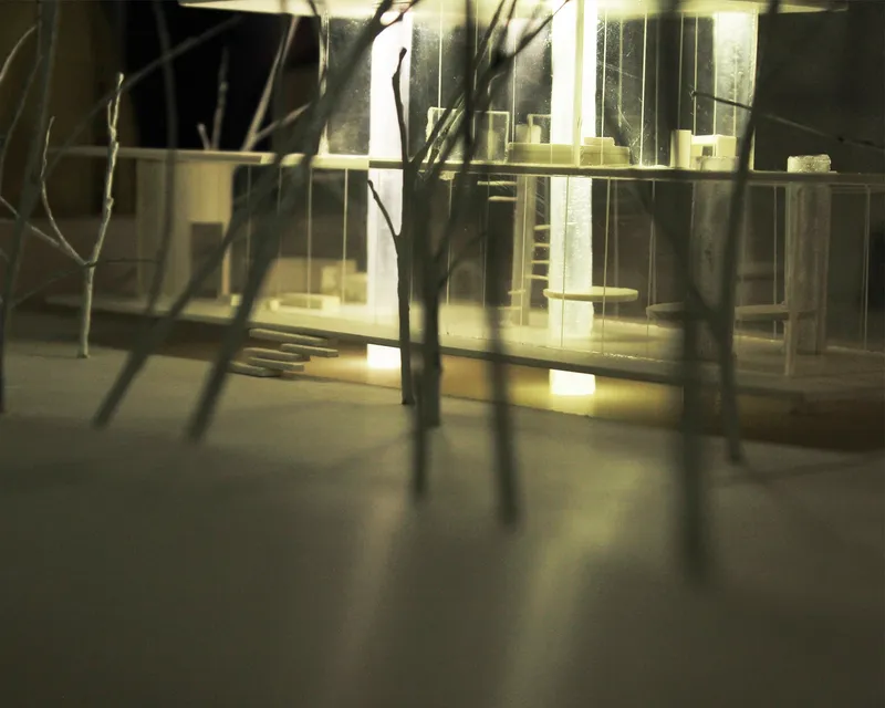 Warm interior lighting reveals the glass-wrapped studio as a glowing retreat within the forest.