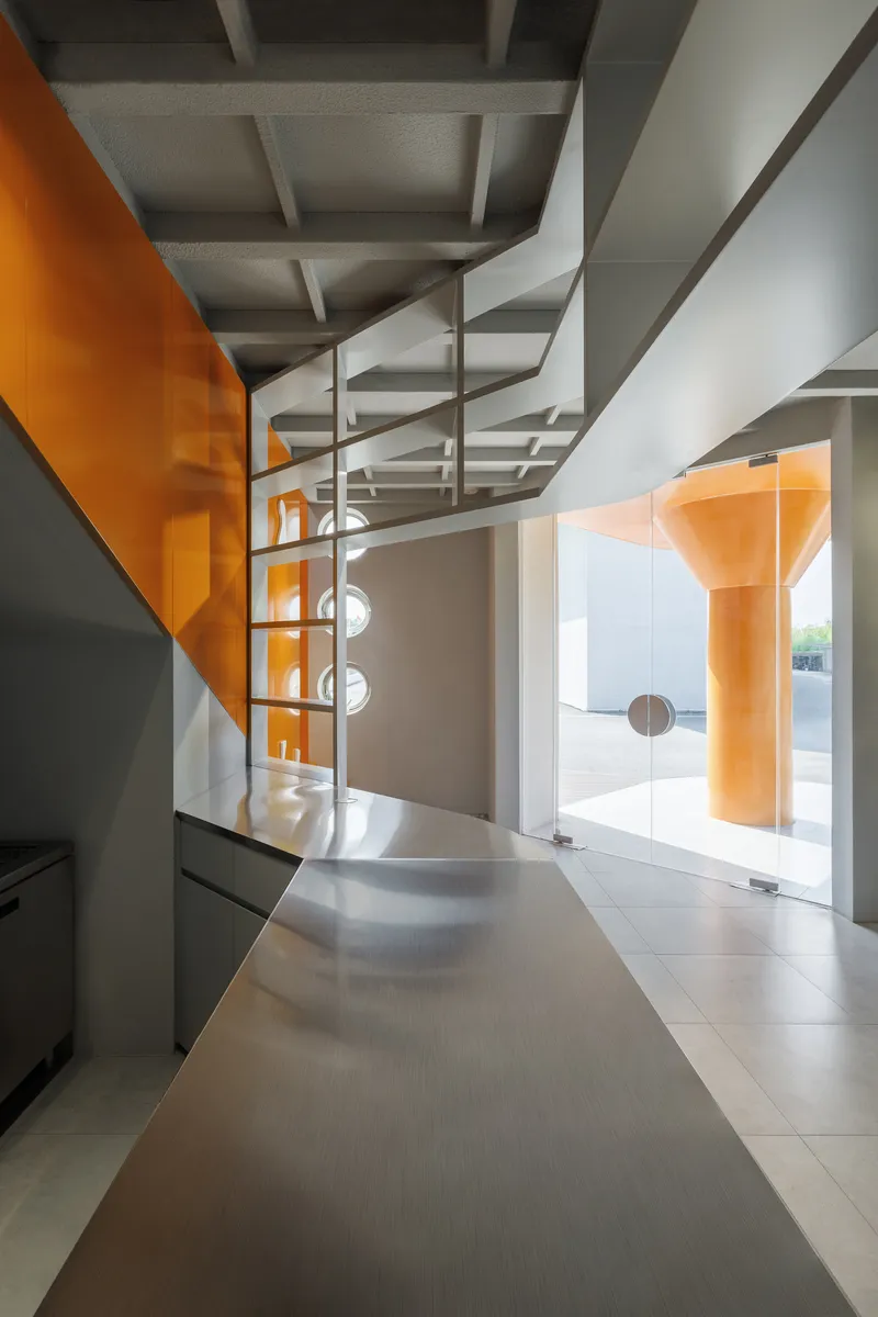 Spiral staircase beneath exposed ceiling beams with orange glass partition reflecting afternoon light
