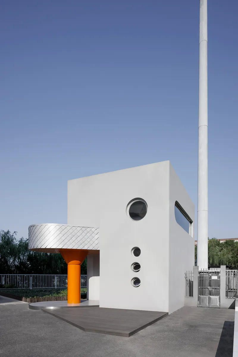 White stucco facade with stacked circular windows and angled glazing beside a white pole in daylight