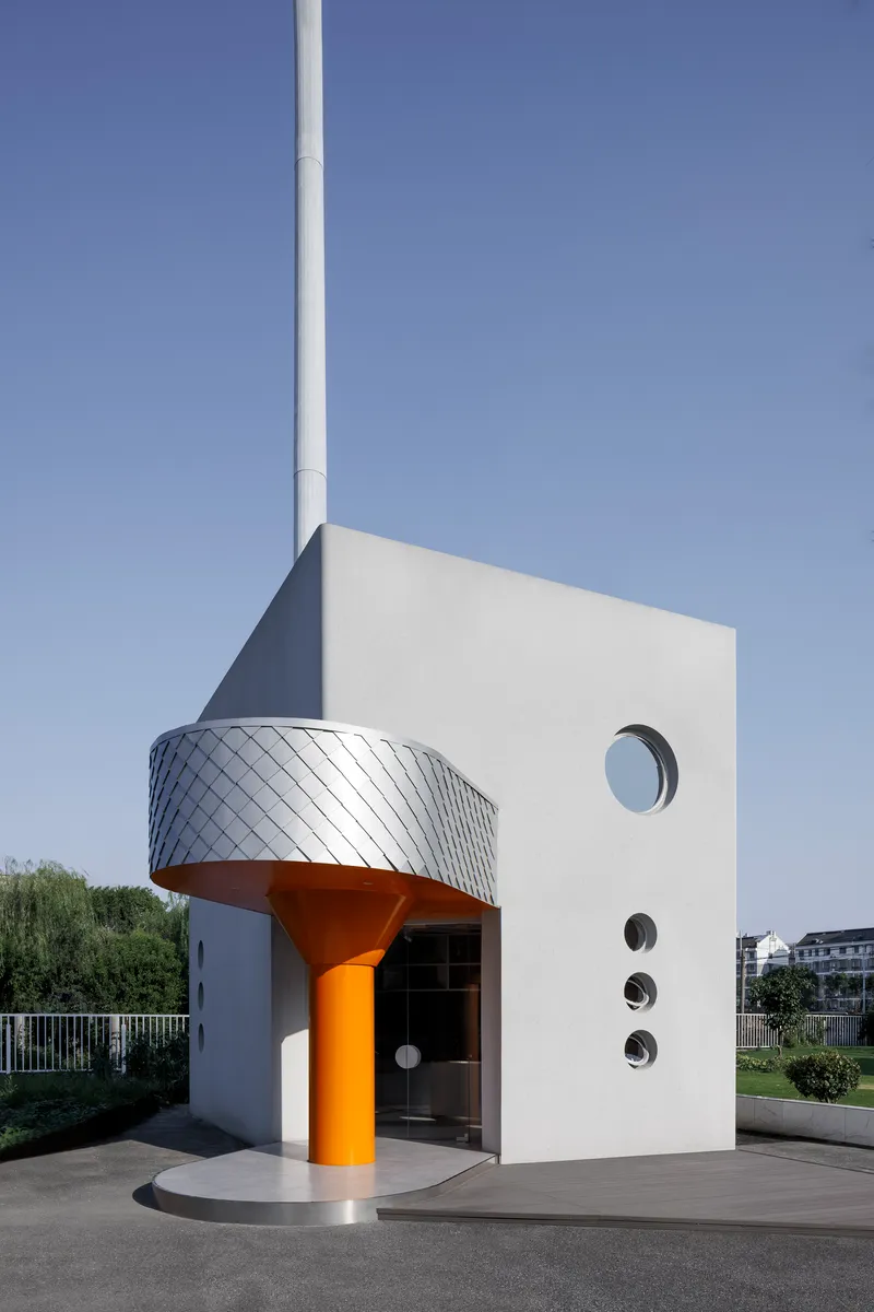White cubic volume with orange column, silver-scaled canopy, and circular porthole windows under clear sky