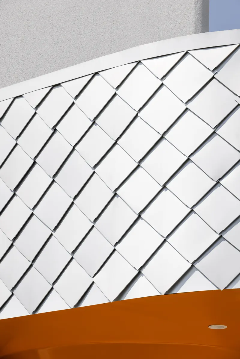 Curved white shingled wall intersecting with orange soffit under bright daylight