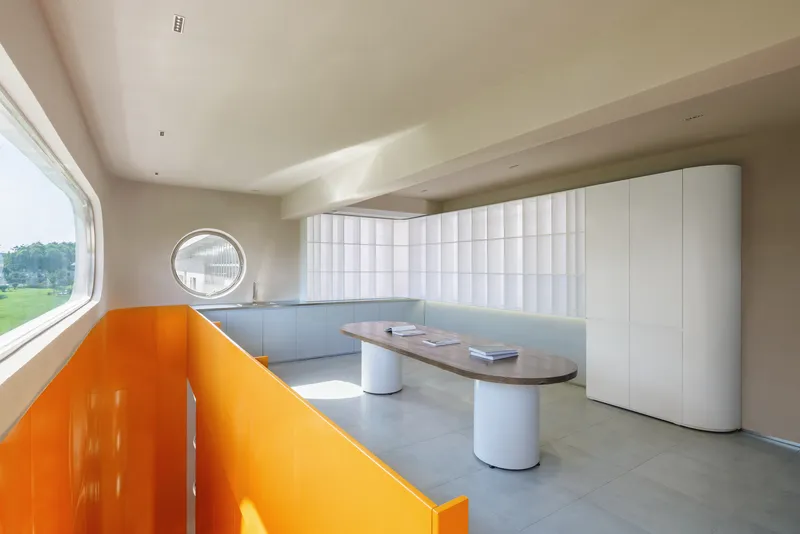 Interior space with orange bench seating, oval table, and white quilted wall panels beneath a circular window