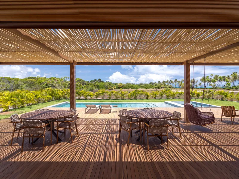 Covered terrace with slatted timber ceiling and wicker furniture facing the pool and lawn beyond