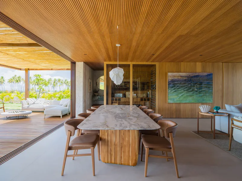 Open-plan dining area with stone-topped table beneath a ribbed timber ceiling and pendant light
