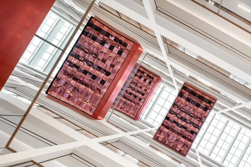 Oblique view of three metallic red tile panels suspended below white structural beams and skylight