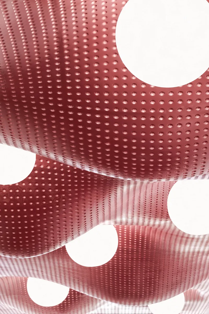Close-up of perforated red metal ceiling panel curving around circular light openings