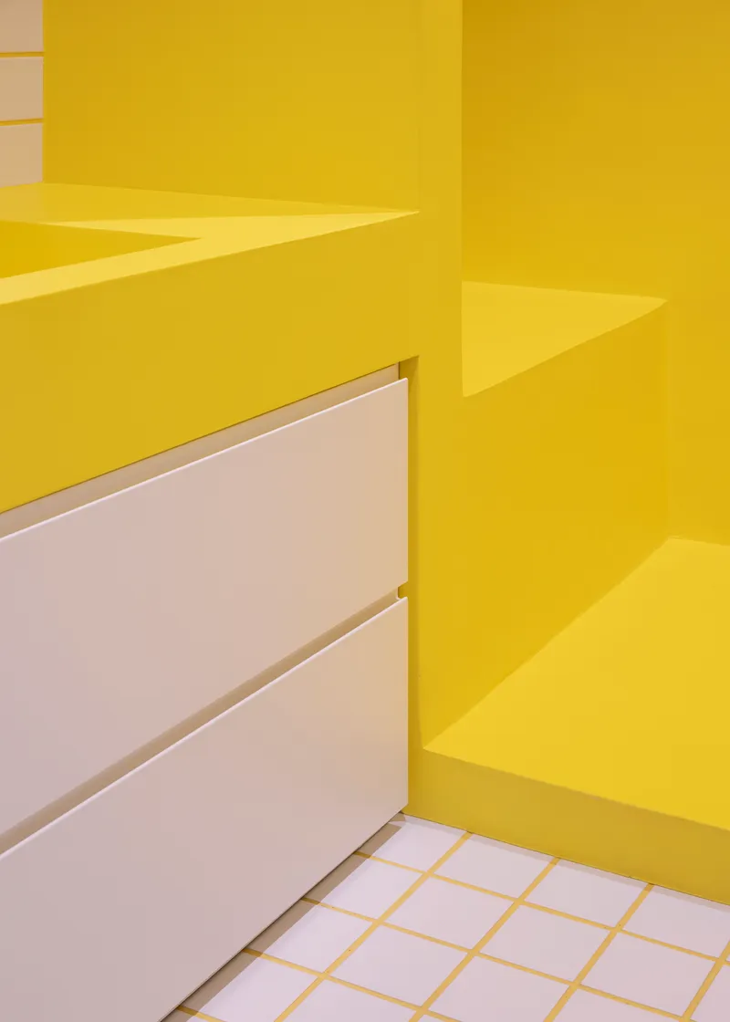 Detail of yellow countertop edge meeting white drawer fronts and grid tile floor