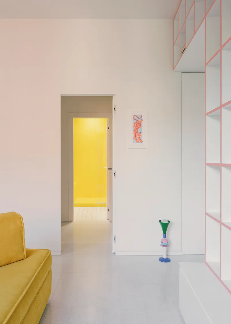 Living room view through doorway to yellow-lit room beyond with pink shelving along the wall