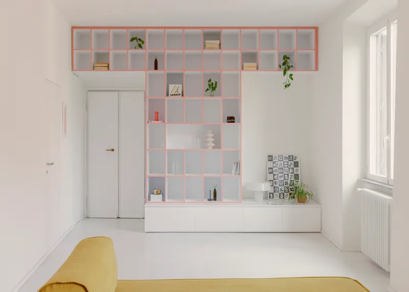 Pink-framed shelving unit with books and plants above white storage cabinetry in bright daylight