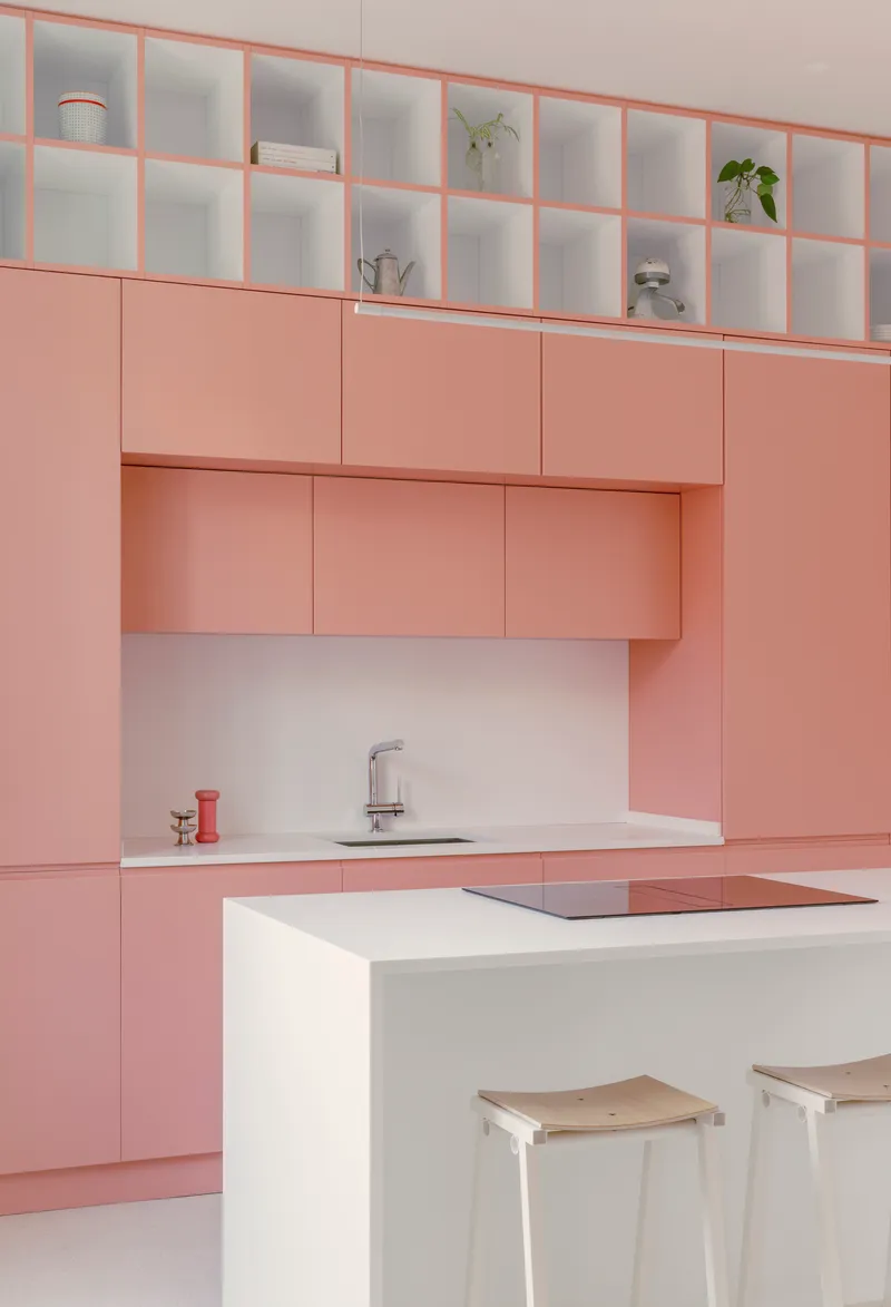 Kitchen with pale pink cabinetry, white island with integrated cooktop, and open shelving above displaying plants