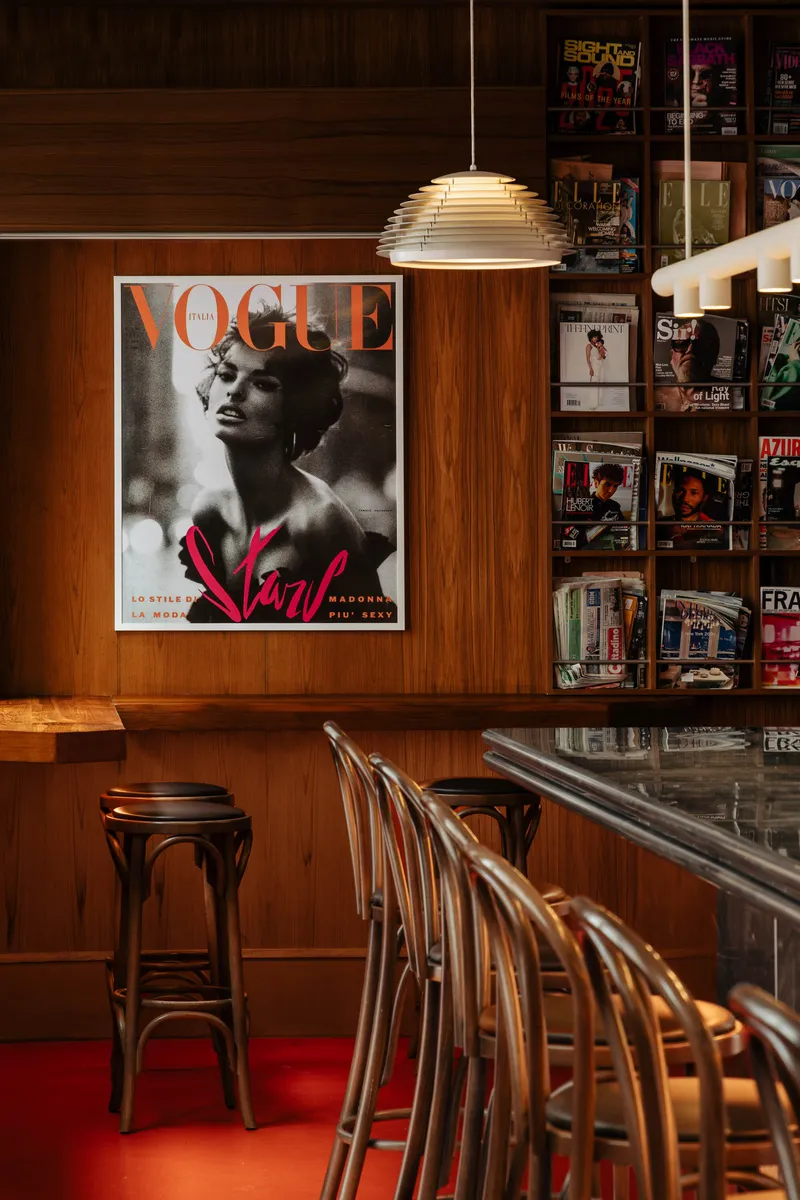 Timber-paneled bar area with bentwood stools, layered pendant light and magazine display under warm lighting