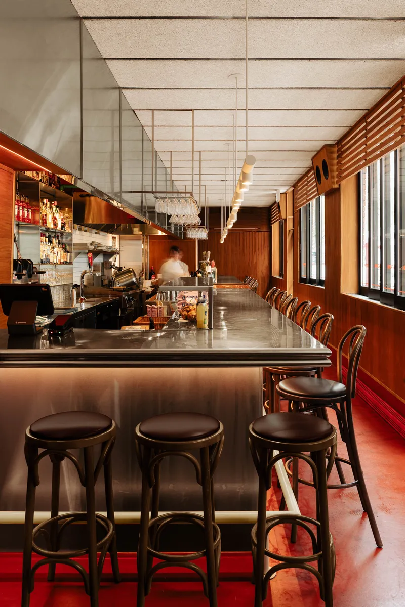 Illuminated bar counter with bentwood stools and wood paneling along the window wall with sunlight