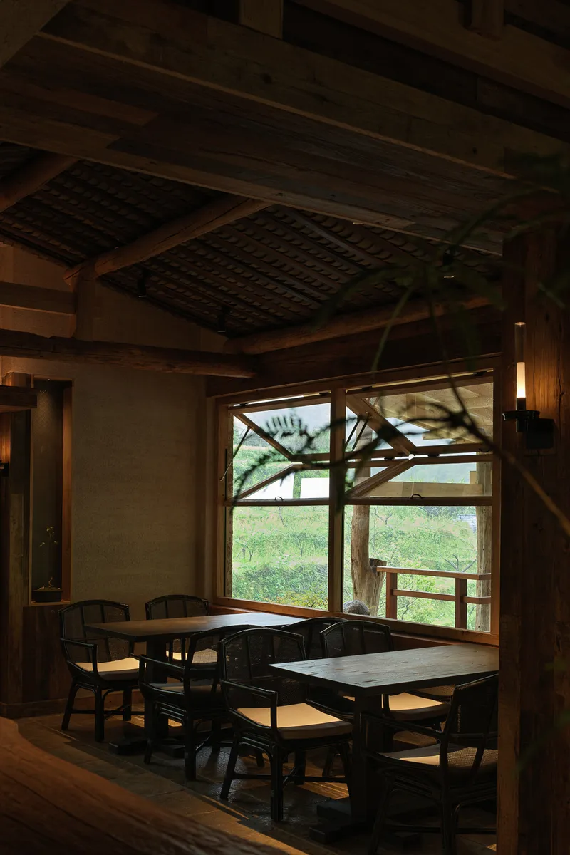 Interior dining area with timber ceiling beams and large window framing views of a terrace and greenery