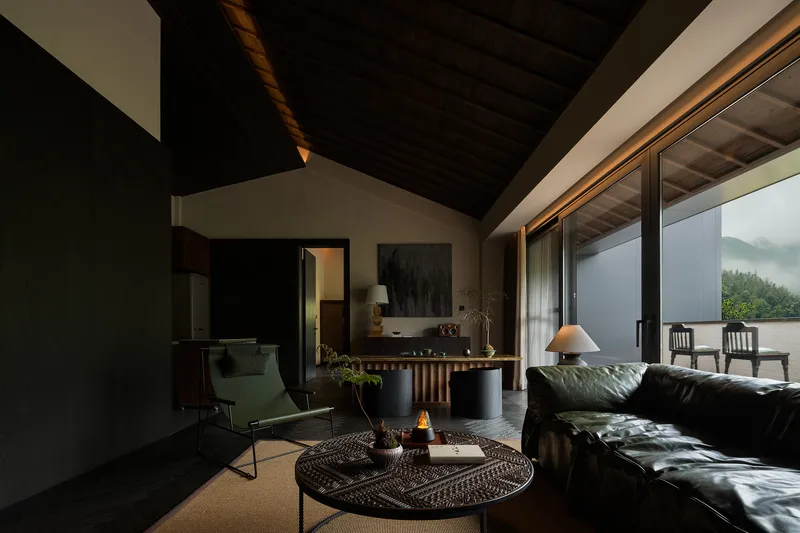 Living room with dark timber ceiling and glazed doors opening to a terrace with misty mountain views