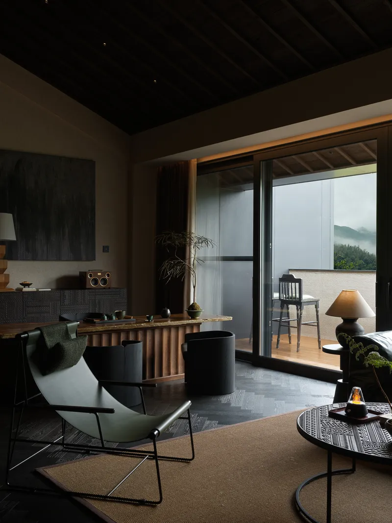 Open living space with fluted timber bar and sliding glass doors framing forested mountains in fog