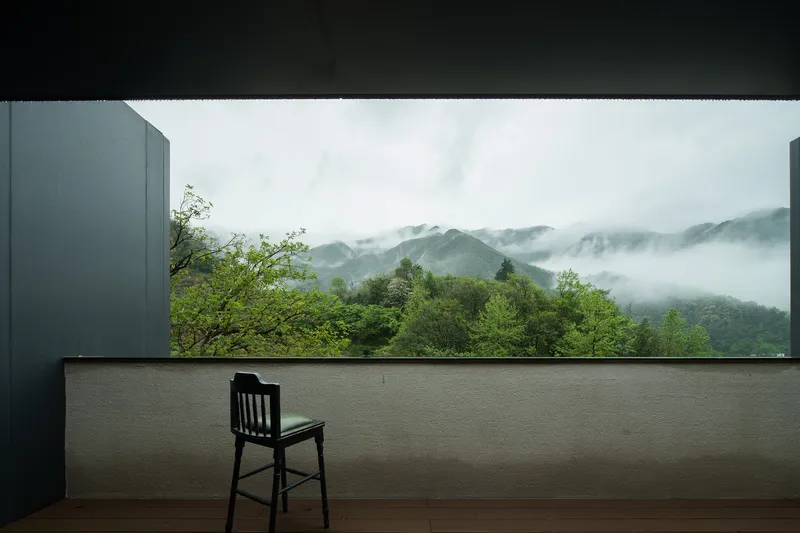 Outdoor terrace with single chair facing cloud-wrapped mountains and dense green forest below