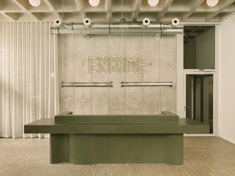 Reception desk with paneled concrete wall displaying dimensional lettering and exposed ceiling ductwork