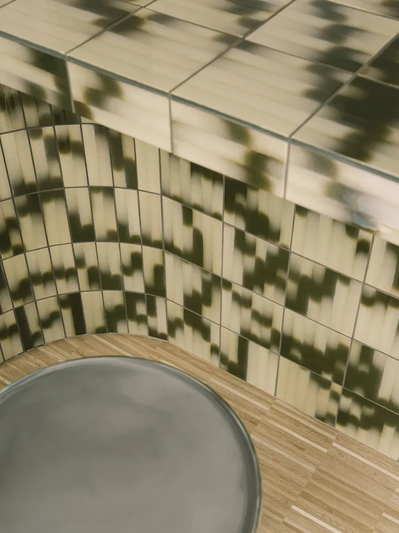 Corner detail of cream-tiled wall with dappled shadow patterns cast across horizontal subway tiles
