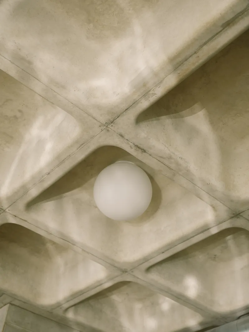 Close-up of one spherical pendant light nested in a concrete waffle slab coffer with shadows