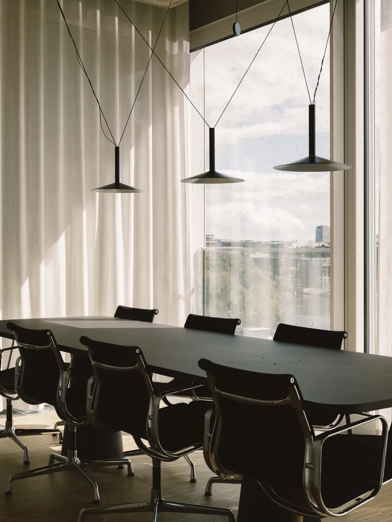 Conference room with three pendant lights hanging above long table facing floor-to-ceiling windows