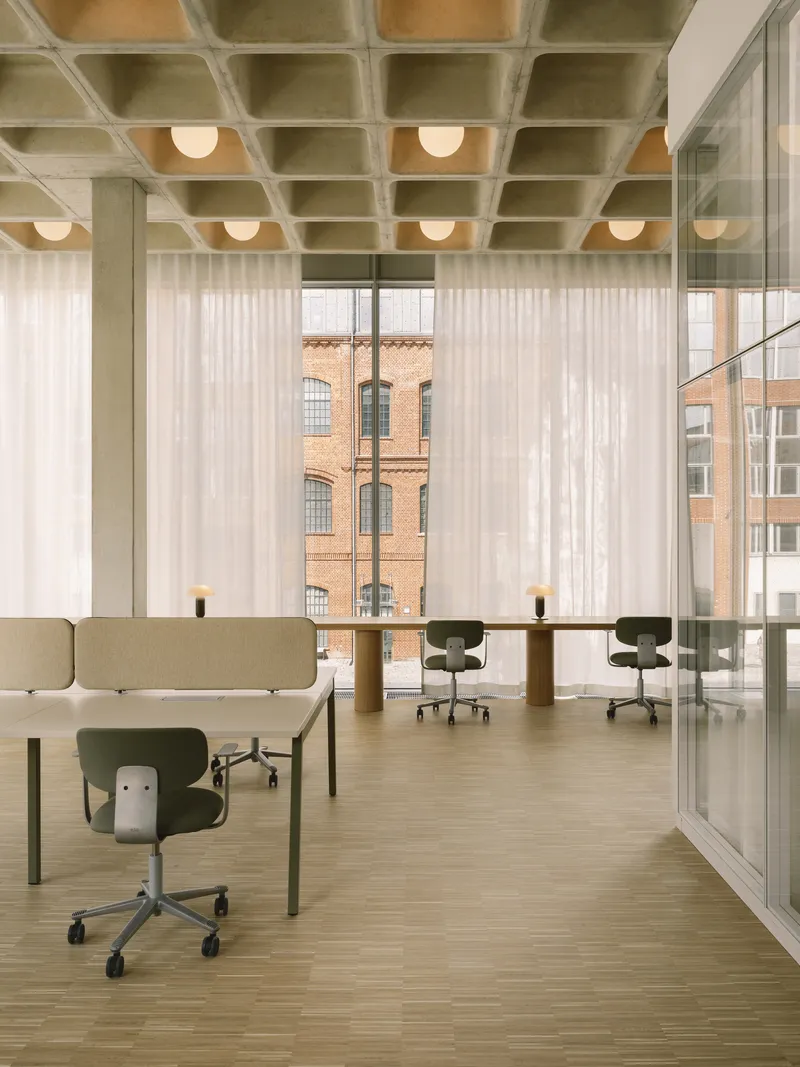 Open office floor with concrete waffle ceiling, sheer curtains filtering daylight and views to brick facade