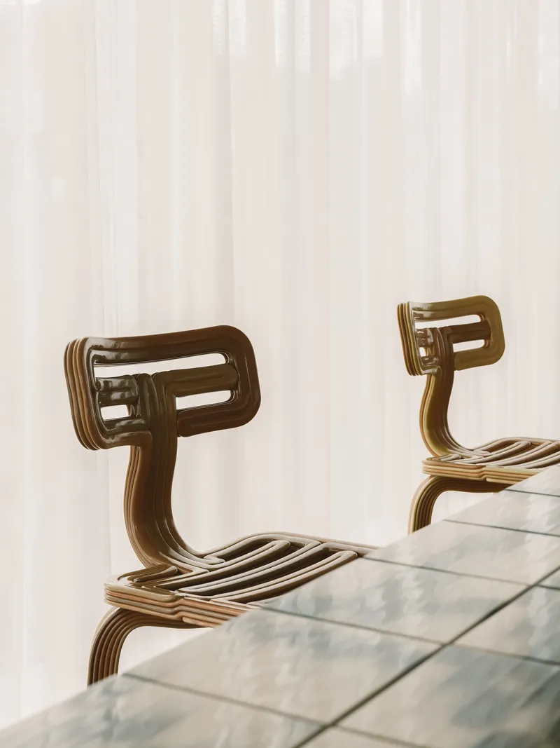 Close-up of two laminated plywood chairs with curved backs beside glass table surface
