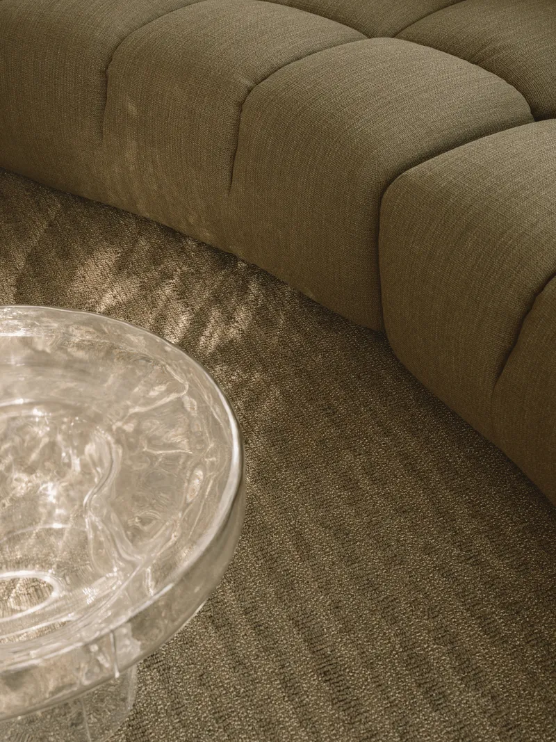 Detail of upholstered sofa edge meeting textured carpet with clear glass coffee table