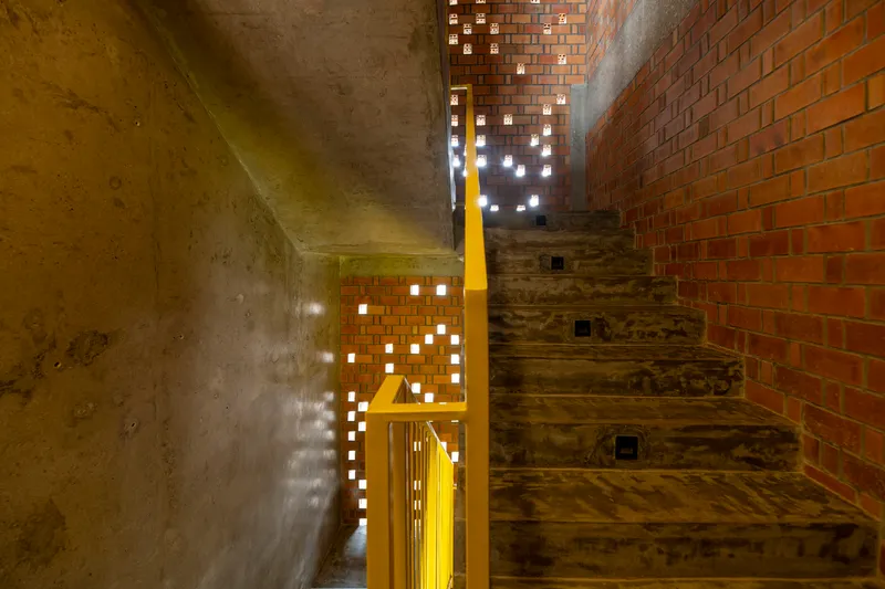 Interior stairwell with patterned brick screen wall casting light through perforations at dusk