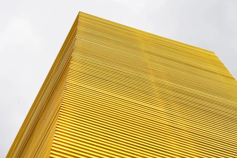 Close-up of the yellow corrugated metal facade corner against an overcast sky