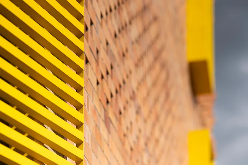 Detail of yellow horizontal louvres meeting a perforated brick wall with yellow accents