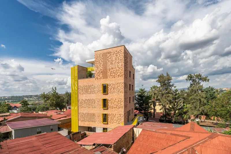 Five-storey brick tower with perforated facade and yellow service column rising above red corrugated roofs