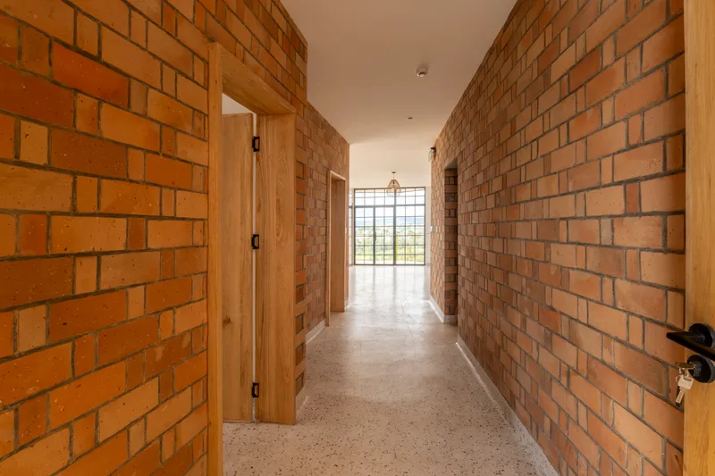 Corridor with exposed brick walls, timber doorframes and terrazzo flooring leading to glazed end wall