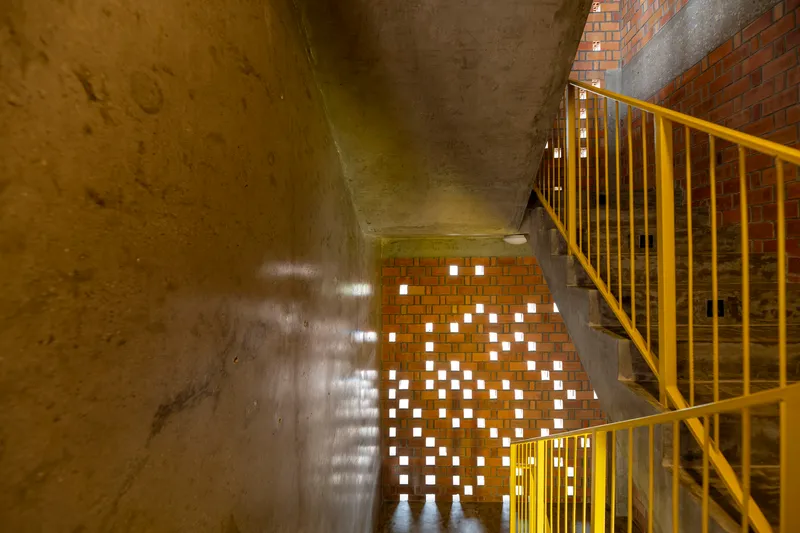 Stairwell with yellow metal railing, concrete walls and perforated brick screen casting light patterns