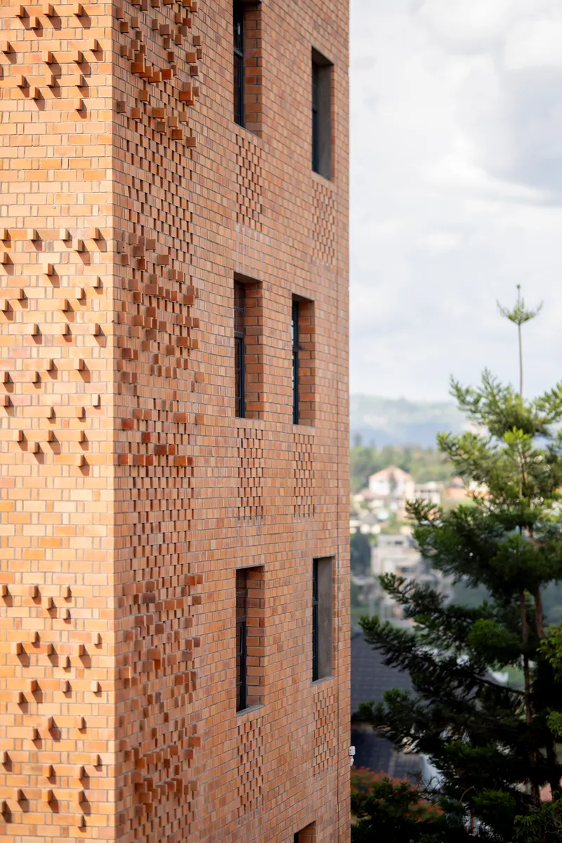Facade detail showing patterned brickwork with protruding headers and recessed window openings beside green trees