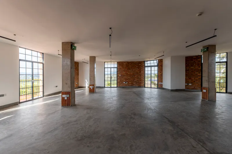 Open floor plan with polished concrete floor, concrete columns and metal-framed windows overlooking green landscape