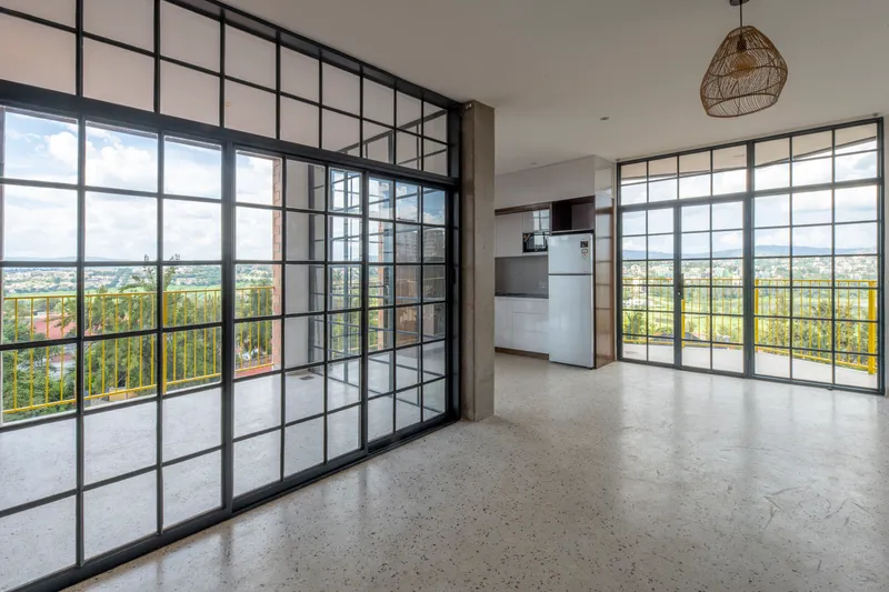 Living area with black-framed glass partition wall and floor-to-ceiling windows opening to terrace with yellow railing