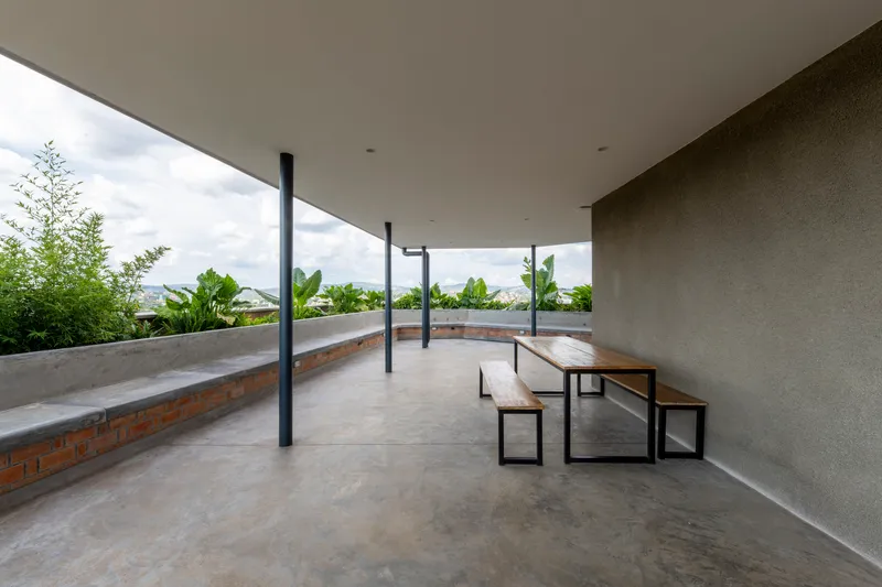 Covered rooftop terrace with curved concrete bench seating, timber picnic table and planted beds under cloudy sky