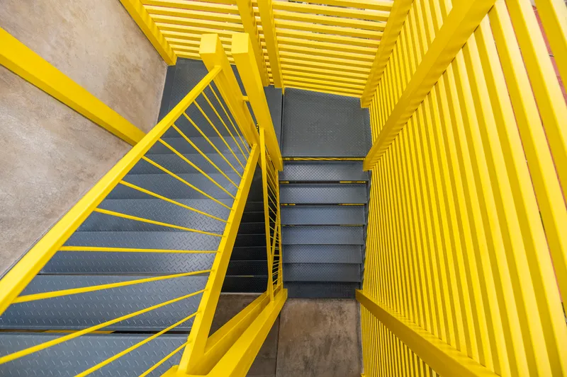 Top-down view of the yellow steel staircase with black treads enclosed by vertical louver screens