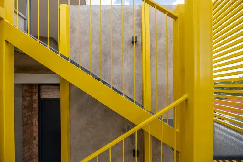 Yellow steel stair with vertical bar railings ascending past concrete and brick walls