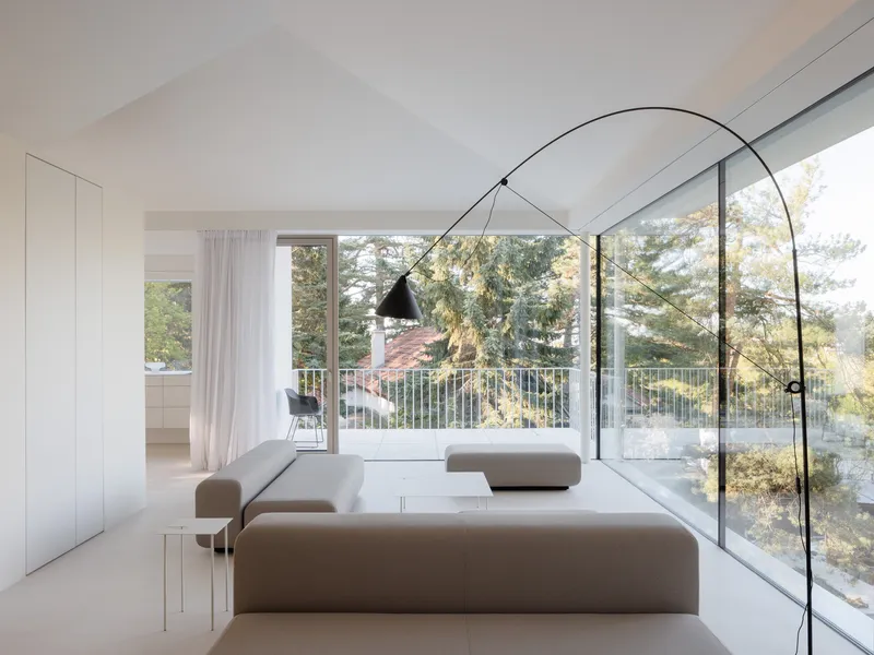 White living room with floor-to-ceiling glazing framing pine trees and a balcony beyond