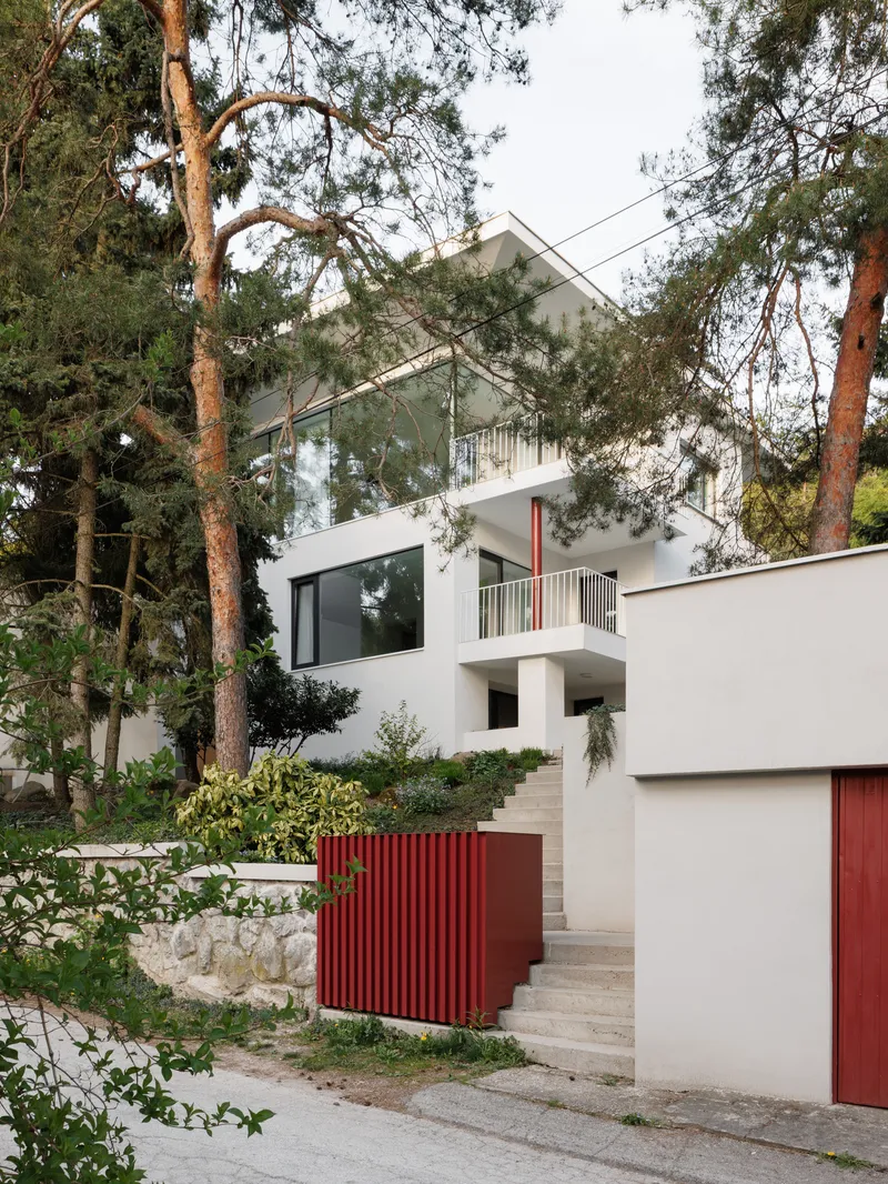 White gabled facade with red corrugated gate panels and stone steps ascending through pine trees