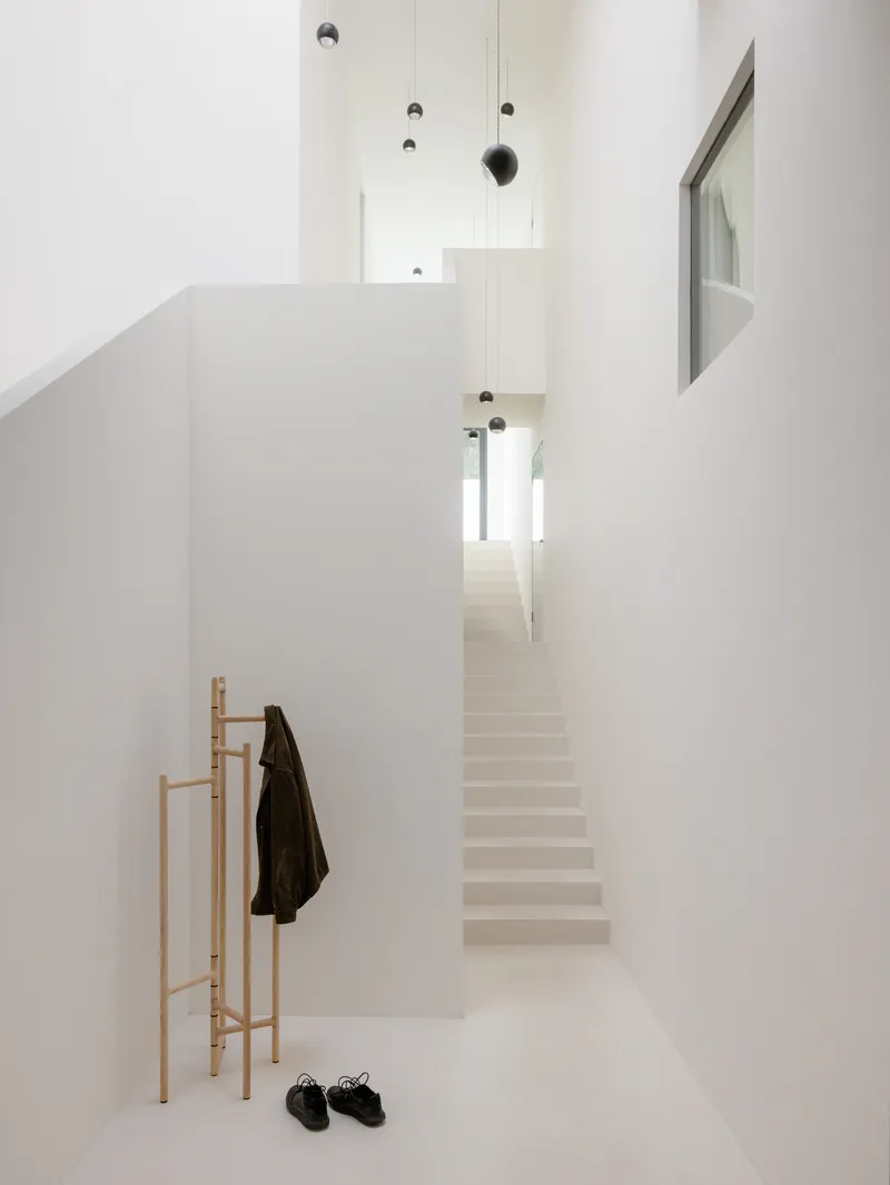 White entry hall with timber coat stand and pale staircase ascending under suspended pendant lights