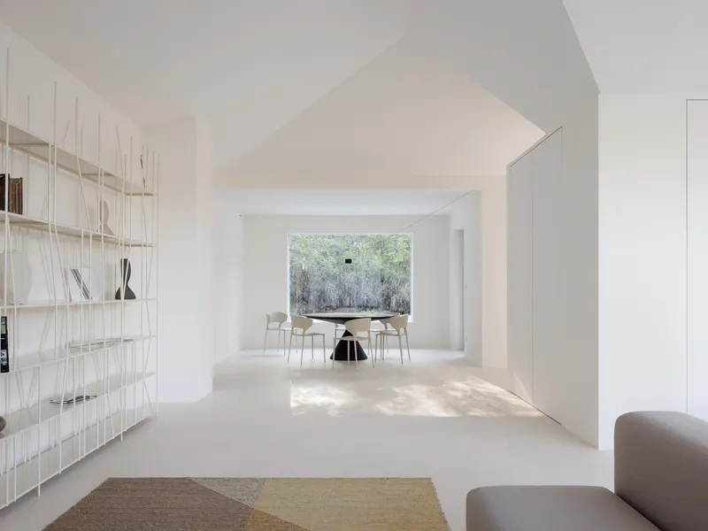 Living space with wire shelving and dining area beyond a large window overlooking winter trees