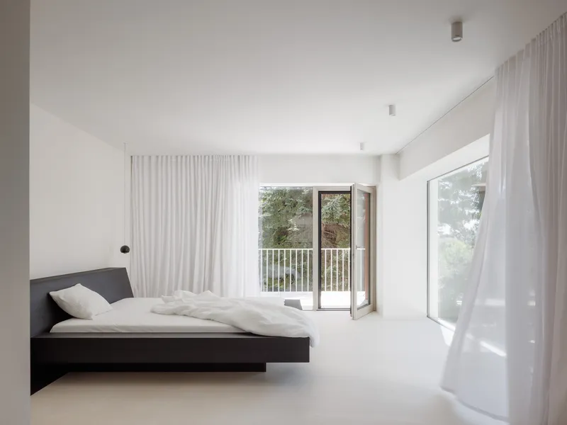Bedroom with black platform bed and sheer curtains flanking glass doors to a railed balcony