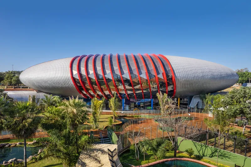 Elevated view of the elliptical ribbed metal roof with red structural bands above landscaped grounds