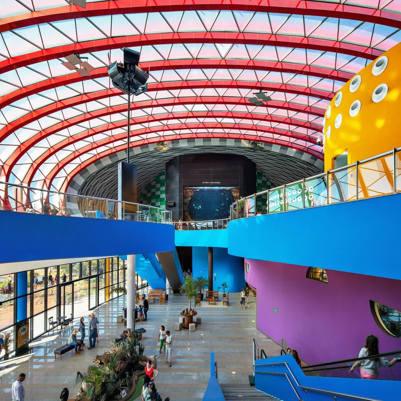 Interior atrium with curved blue and purple balconies beneath a glazed red steel rib structure